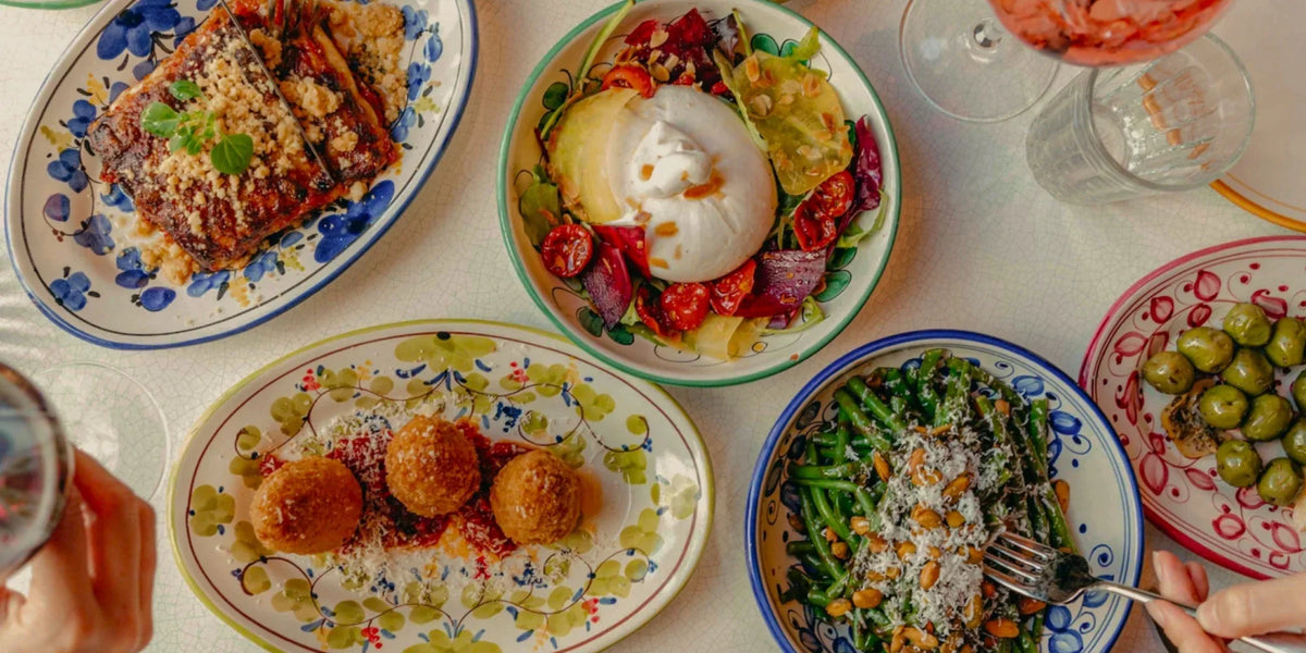 Table de restaurant italien dressée avec des assiettes en céramique peintes à la main, pâtes et antipasti à partager